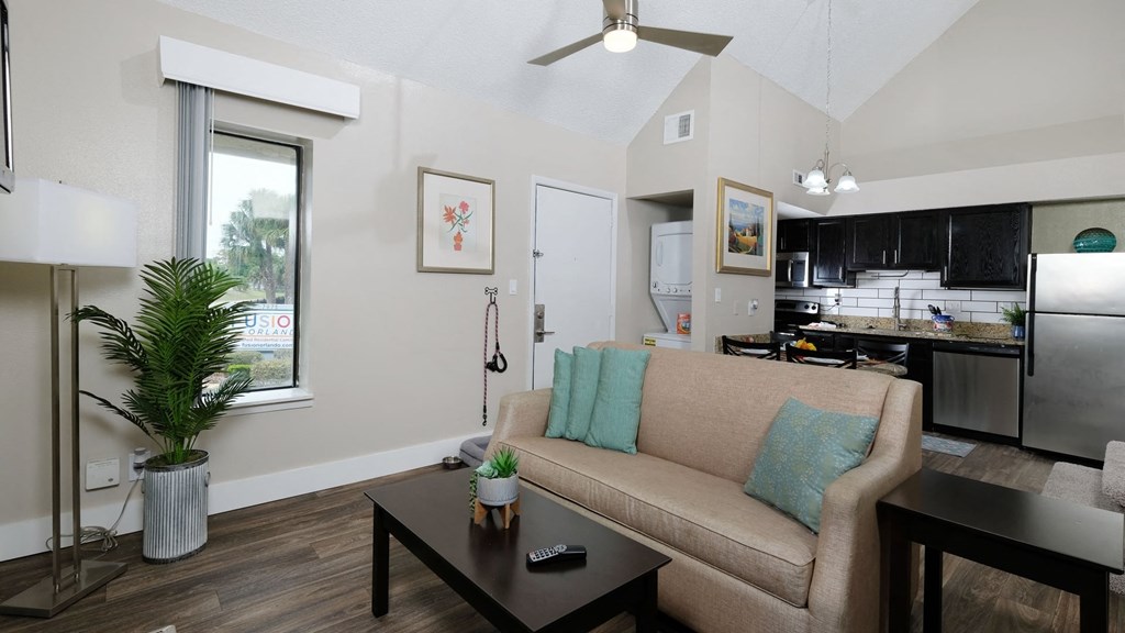 Fusion Orlando furnished studio apartment open concept kitchen and living area with in unit laundry and large window with vertical slat blinds.