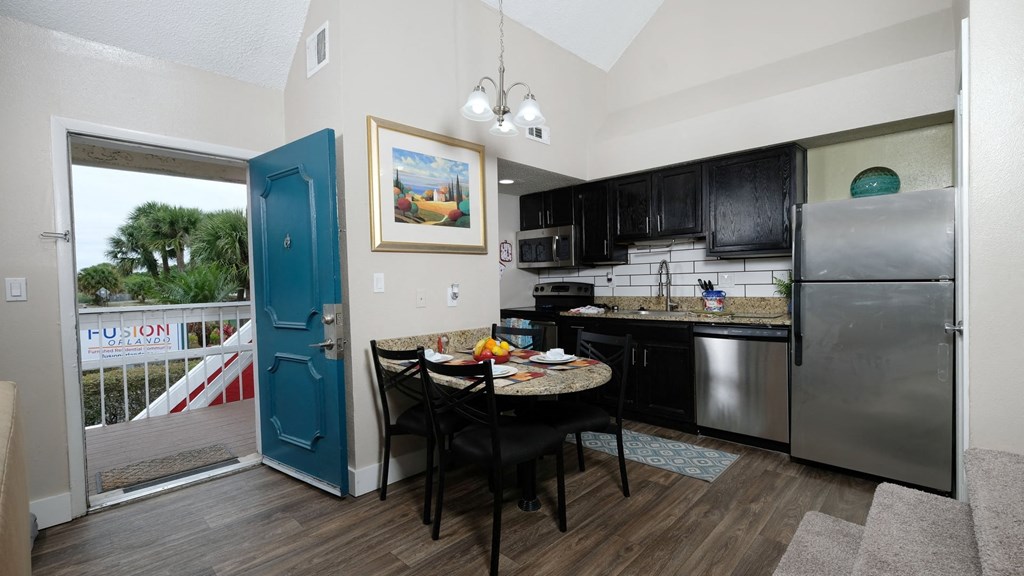 Fusion Orlando single bedroom apartment in Orlando second story apartment kitchen and dinette next to teal front door open to balcony with white railing.