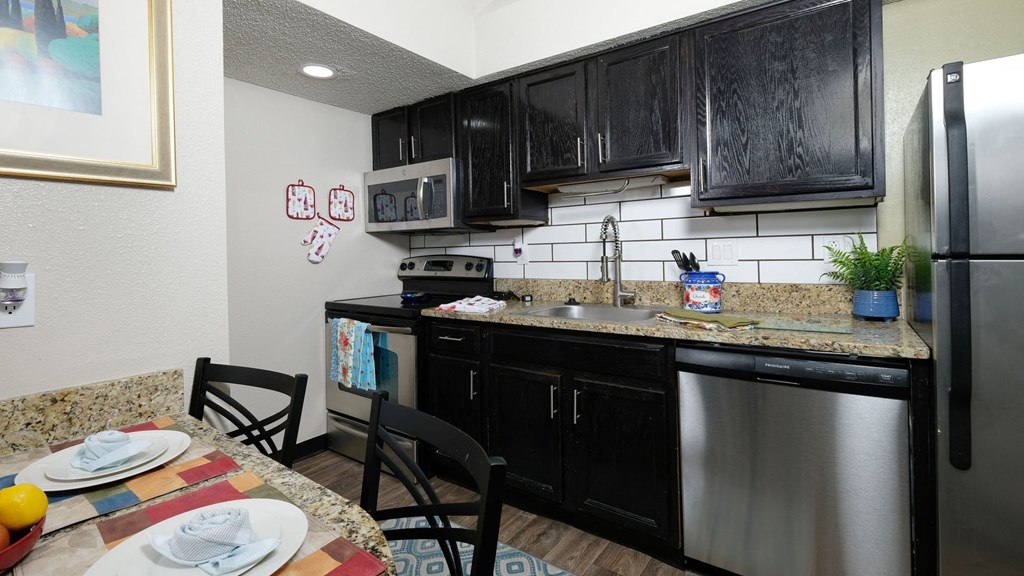 Fusion apartment for rent Orlando apartment kitchen with espresso cabinets, stainless steel appliances, and white tile backsplash.