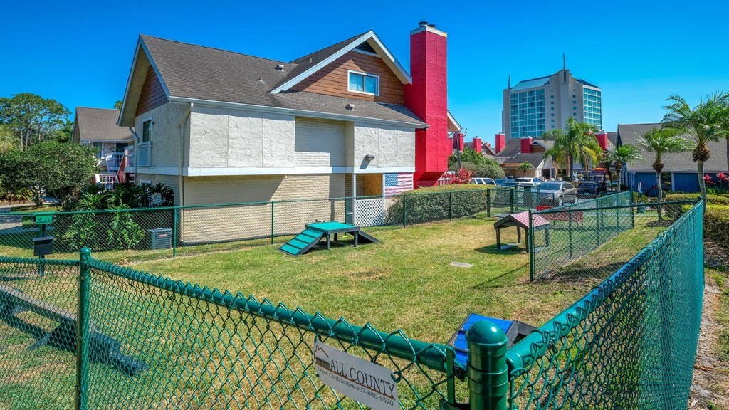 Fusion Orlando apartments dog park with green chain link fence, real grass, dog agility run equipment, and pet waste station.