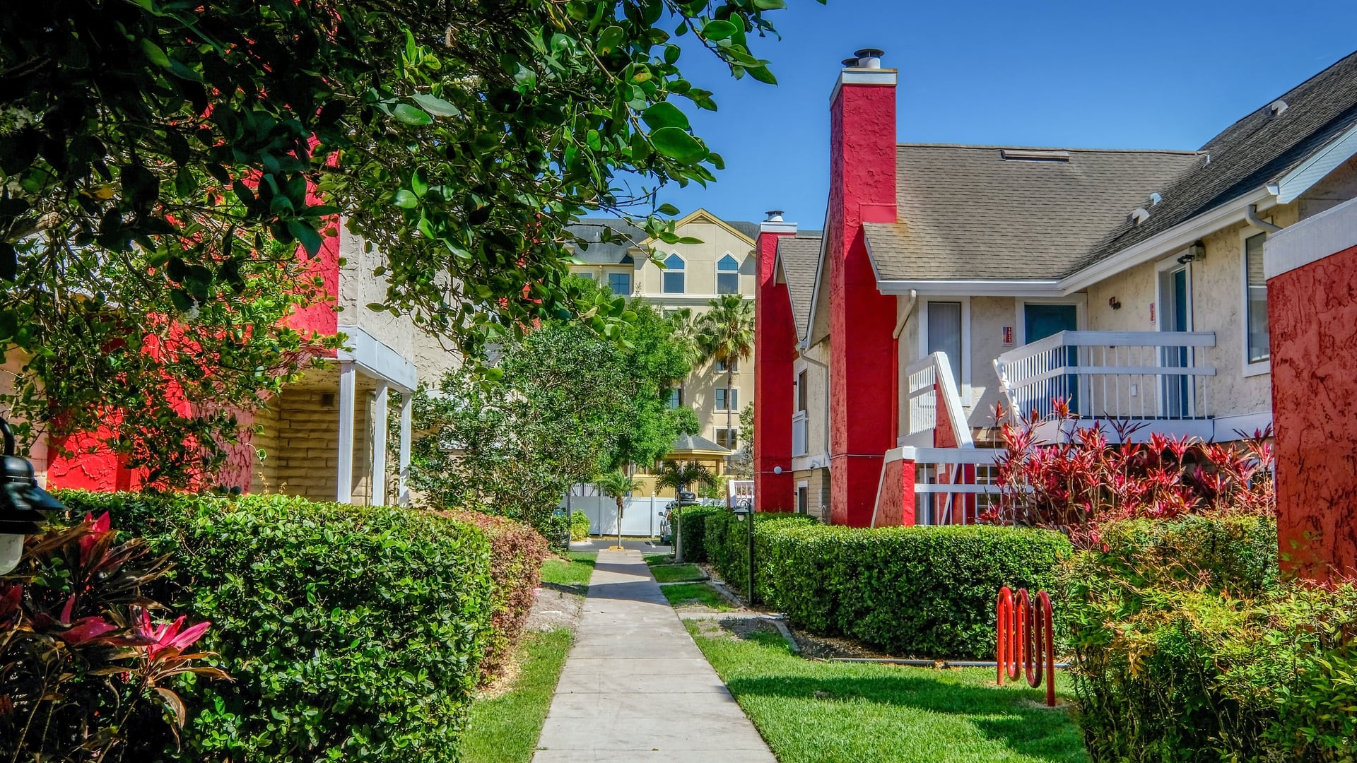 Fusion Orlando apartments pathway lined with lush landscaping and two story apartment buildings with red chimneys and outdoor stairs.