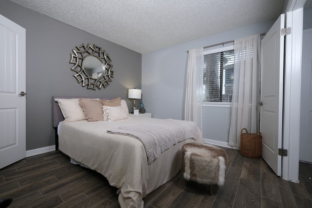 Fusion Fort Worth apartment in Haltom City bedroom with large window with gauze drapes and large bed with cozy bedding and modern fur footstool.