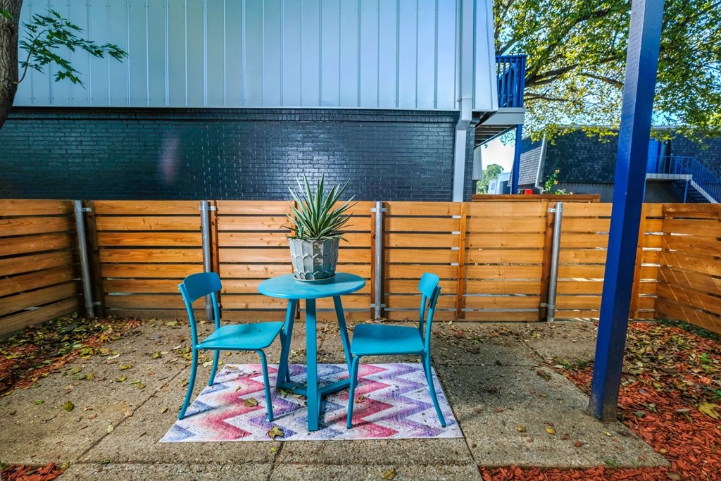 Arlington Studio 700 ground floor apartment patio. Patio has stained wood fence, concrete slab flooring, and blue patio dinette set.