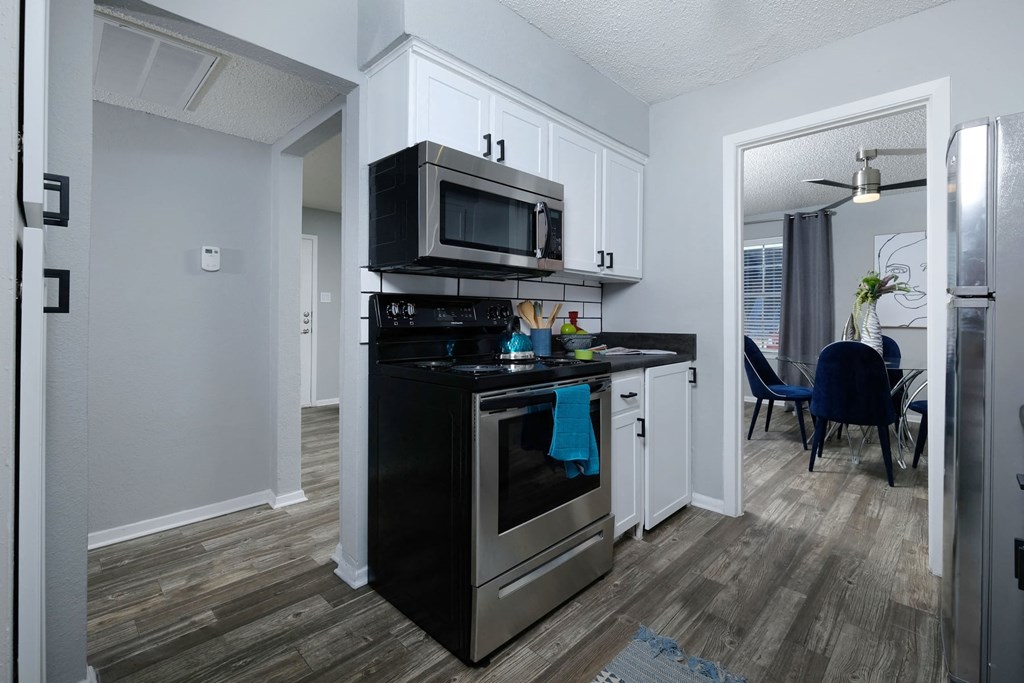 Stadium 700 apartment kitchen with stainless steel microwave, electric stove, and open doorways to modern dining room and hallway.
