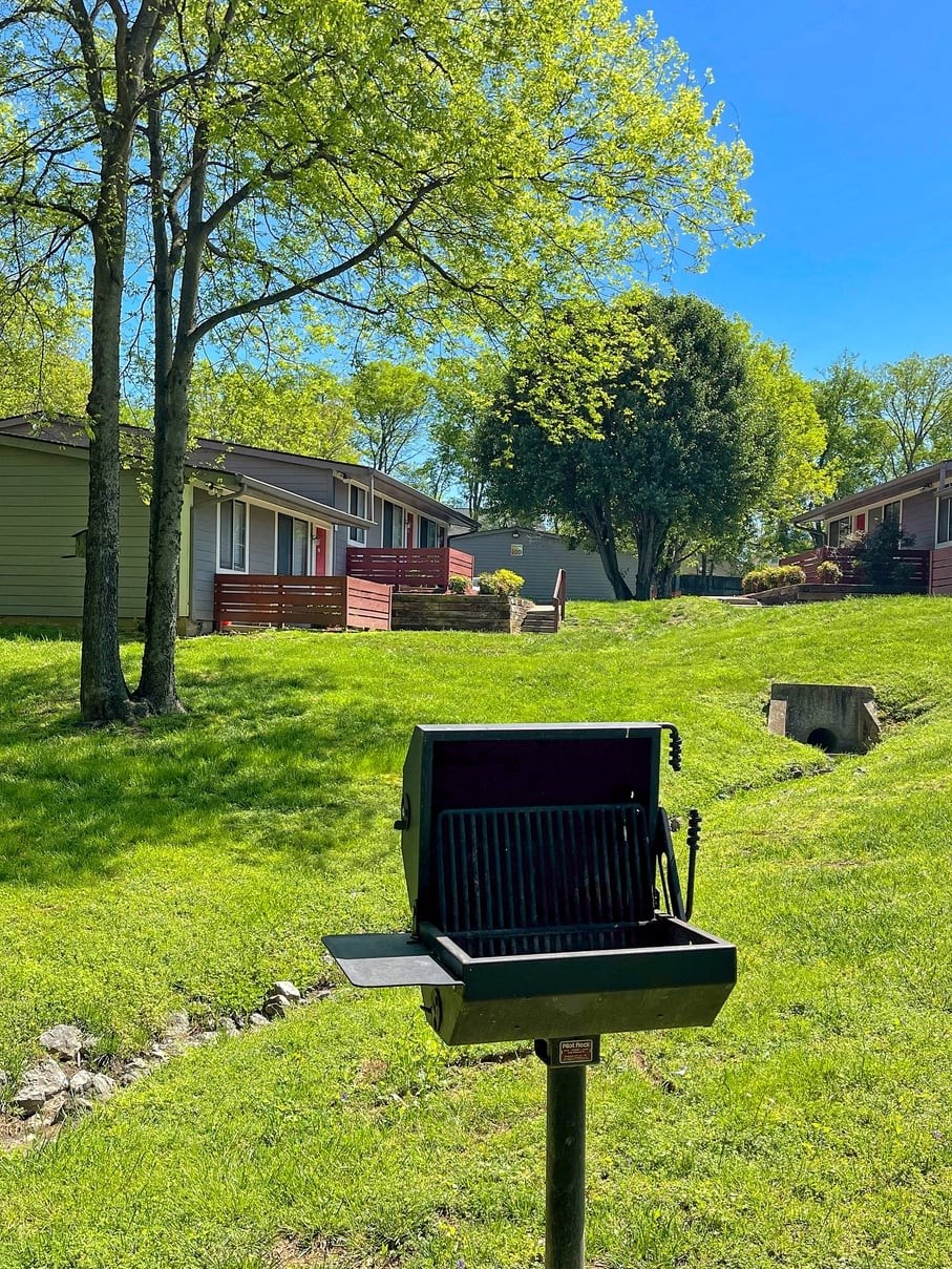 view from barbecue at The Retreat at Indian Lake in Hendersonville: apartment buildings in lush green field with small drainage pipe.