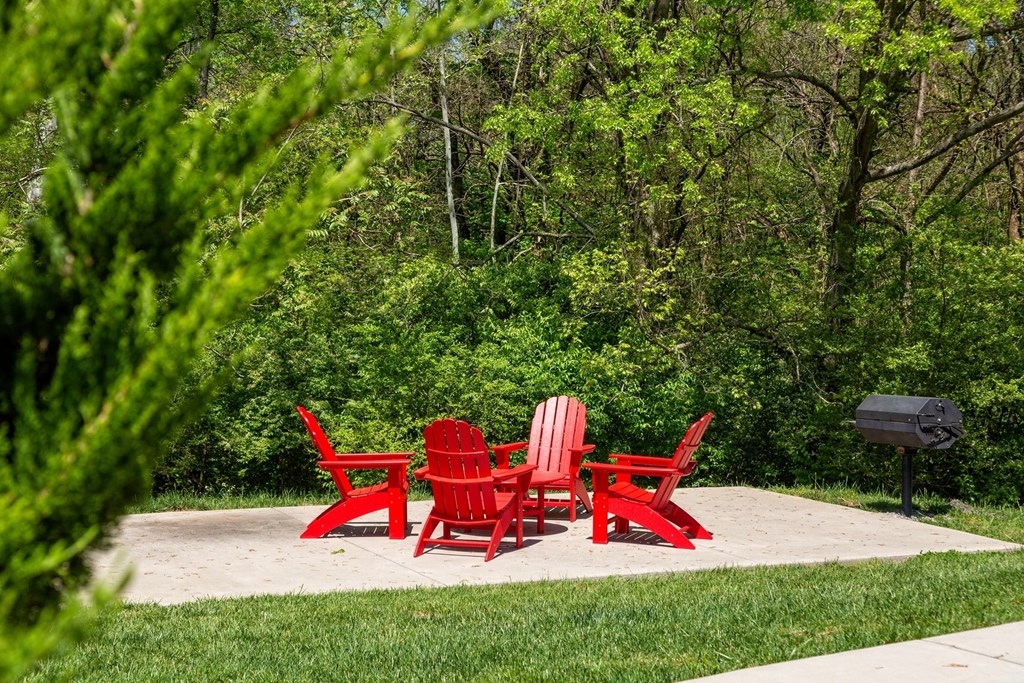 The Retreat at Indian Lake in Hendersonville outdoor seating area with four red Adirondack chairs and barbecue on concrete slab.