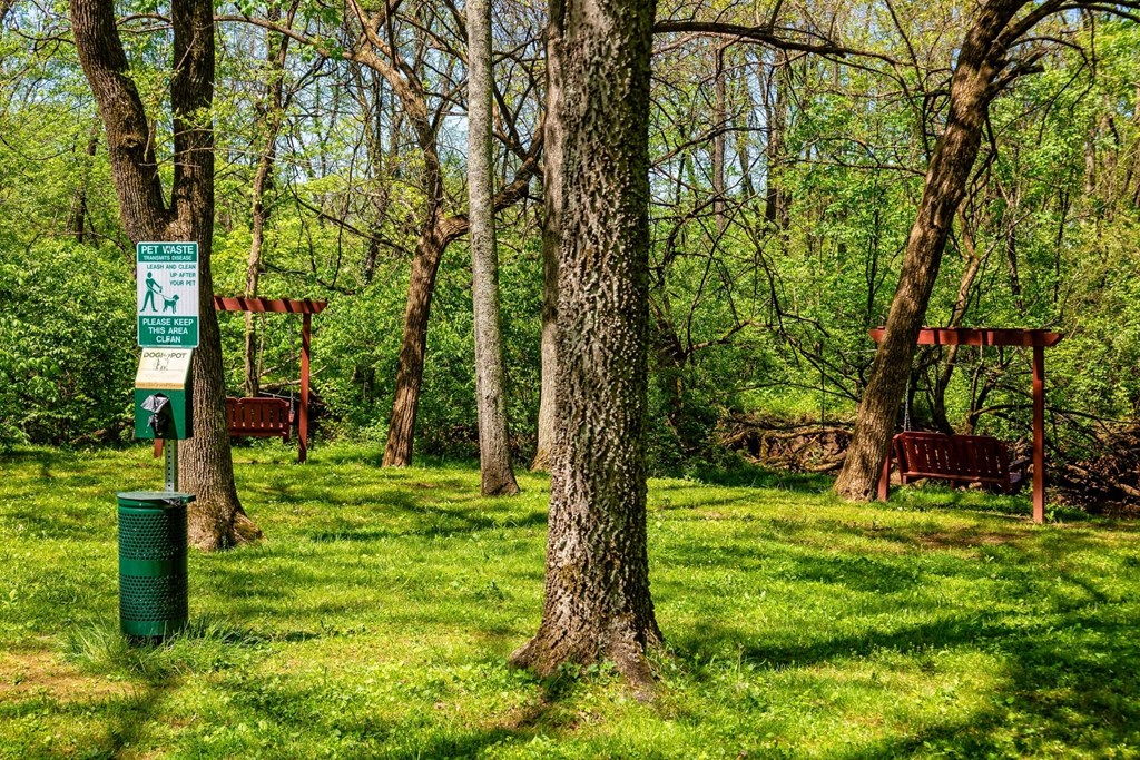 Dog area at The Retreat at Indian Lake in Hendersonville with pet waste station and wooden bench swings amidst tall trees in green grass.