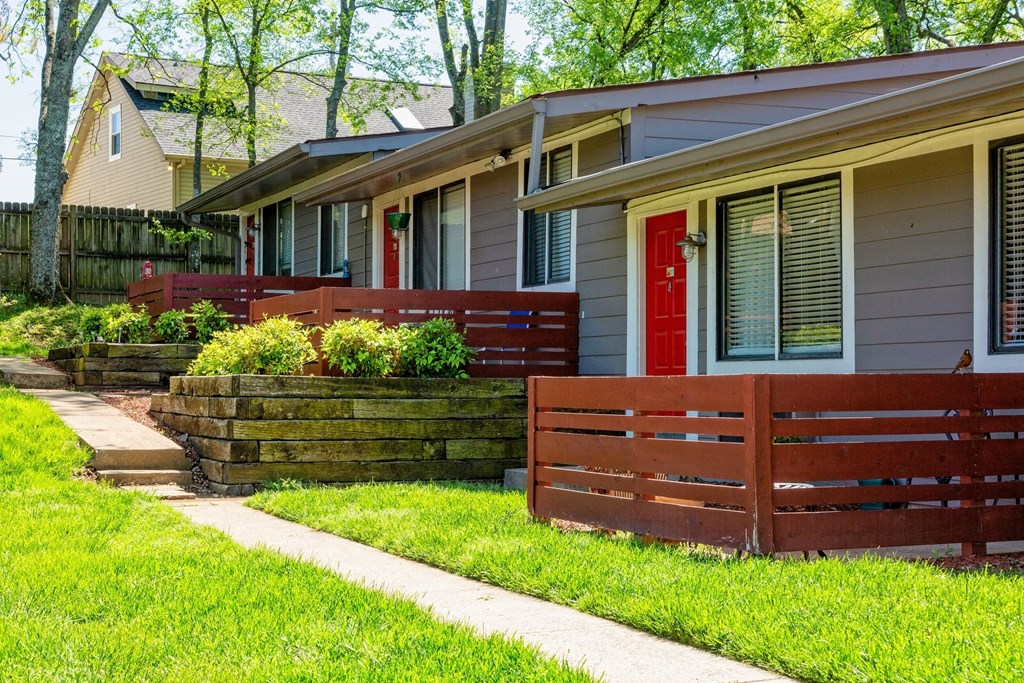 Row of apartments at The Retreat at Indian Lake in Hendersonville with red front doors, grey siding, and green landscaping.