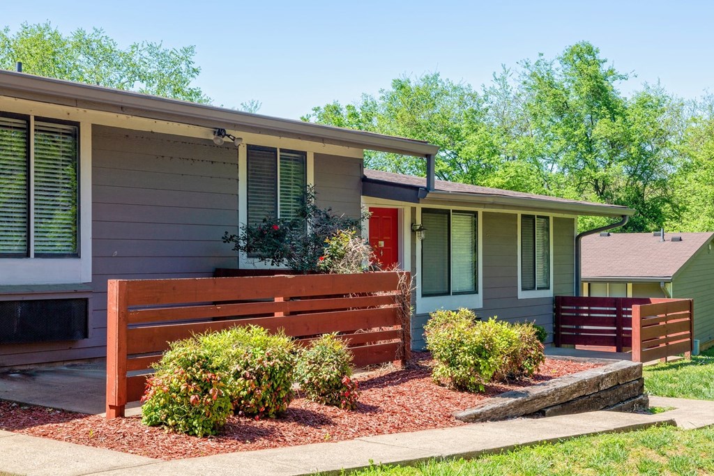The Retreat at Indian Lake in Hendersonville exterior. Apartments are single story with grey siding, red front door, and stained wood fence on patios.