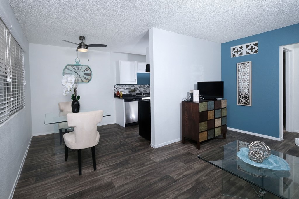 Fifteen Fifty apartments Las Vegas open concept dining room and living area with grey wood tile floors and modern glass dining table and cream cloth chairs.