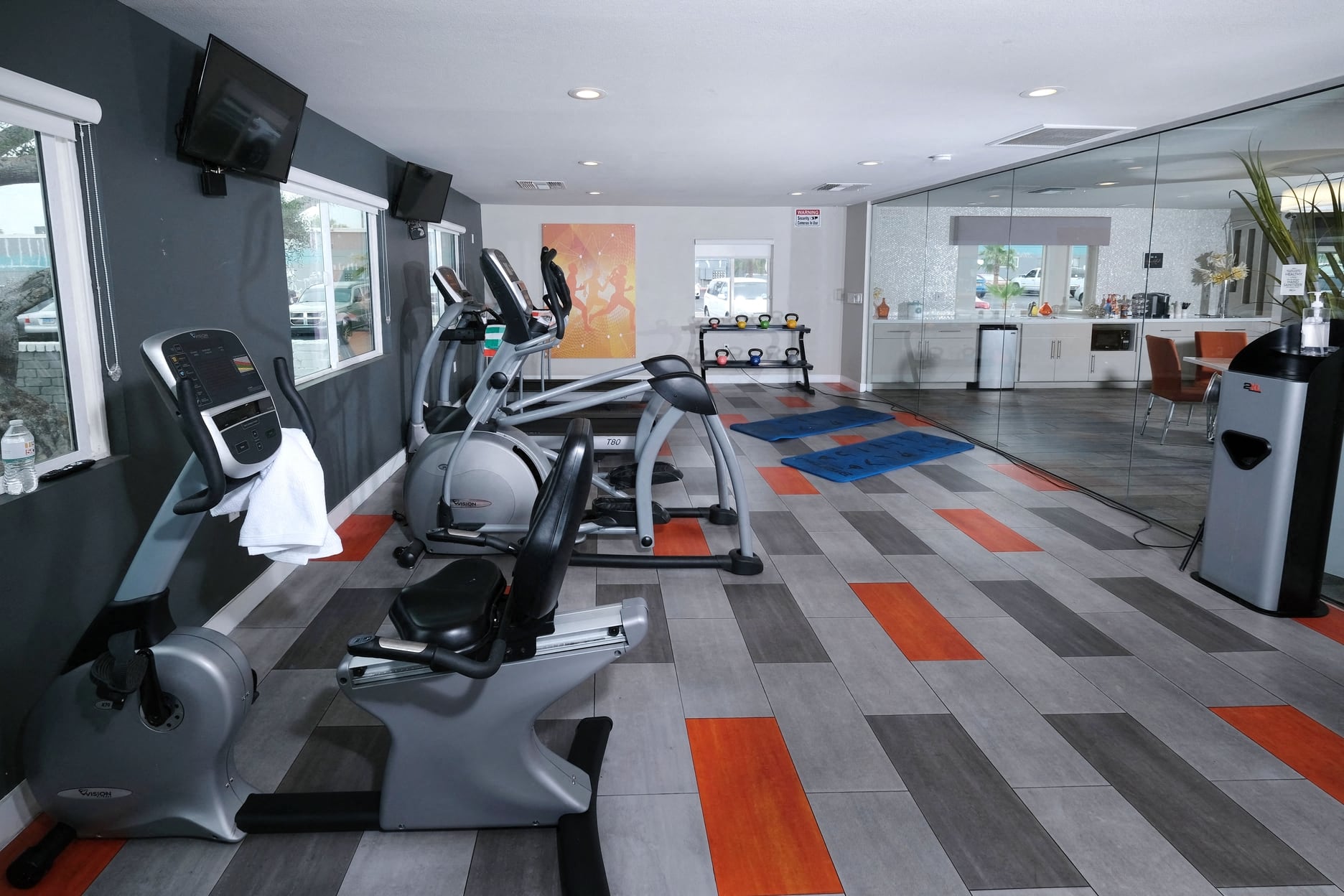 Fifteen 50 apartments near Las Vegas strip on site fitness center with modern orange and grey tile floor and exercise equipment facing wall TVs.