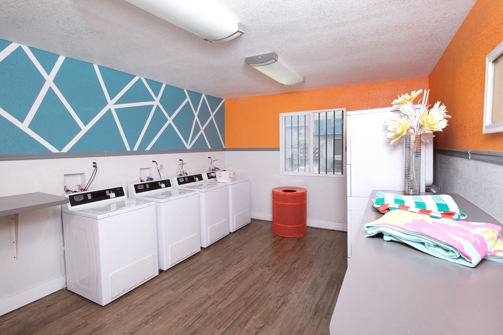On site laundry at Fifteen 50 apartments in Las Vegas, 89119 with four washers and dryers, red trash can, and laundry folding counter.