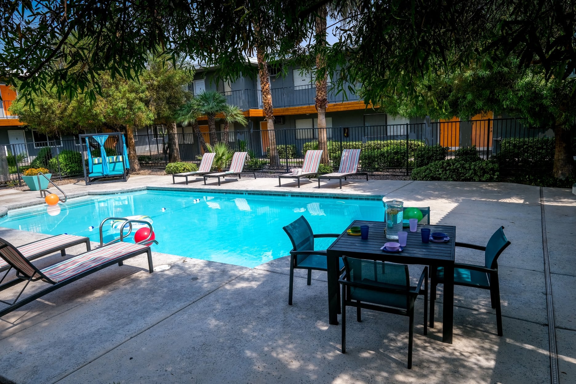 Fifteen 50 apartments near Las Vegas strip Community pool surrounded by tall gated fence, greenery, and patio loungers.
