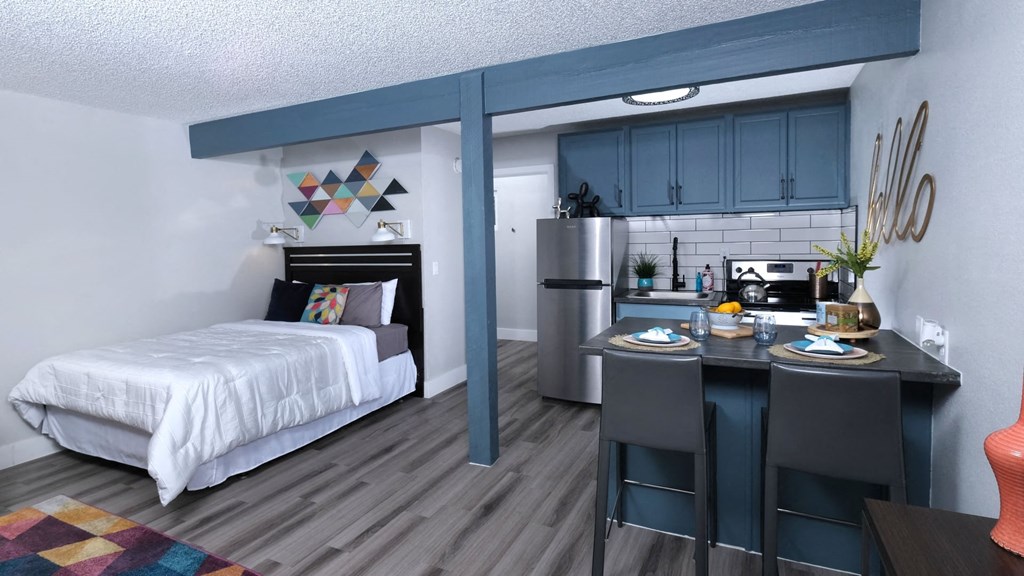 Fusion Las Vegas studio apartment bedroom and kitchen area with navy blue cabinets, stainless steel appliances, and two seater island.