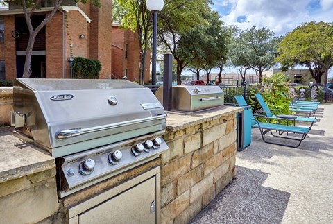 A BBQ grill is on a patio with a blue chair and a brick wall at 1601 Eastchase Pkwy in Fort Worth, TX.