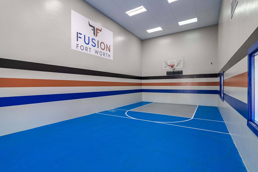 indoor basketball and racquetball court at fusion Fort Worth apartments with blue floor and apartment logo on the wall