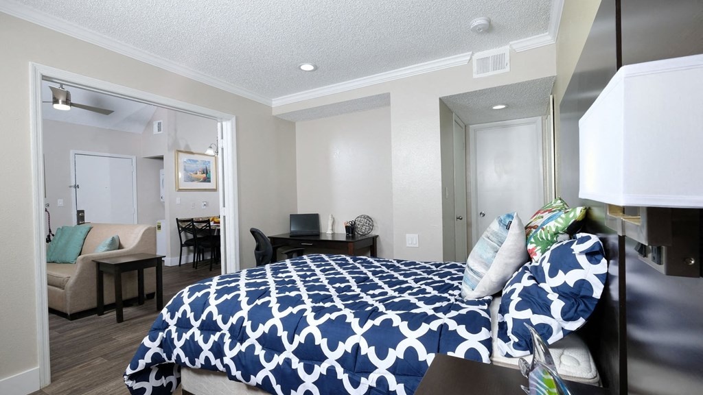 Fusion Orlando furnished apartment bedroom with large open door to living area. Bedroom has large bed with blue and white duvet and desk nook. Apartments in Orlando, FL.