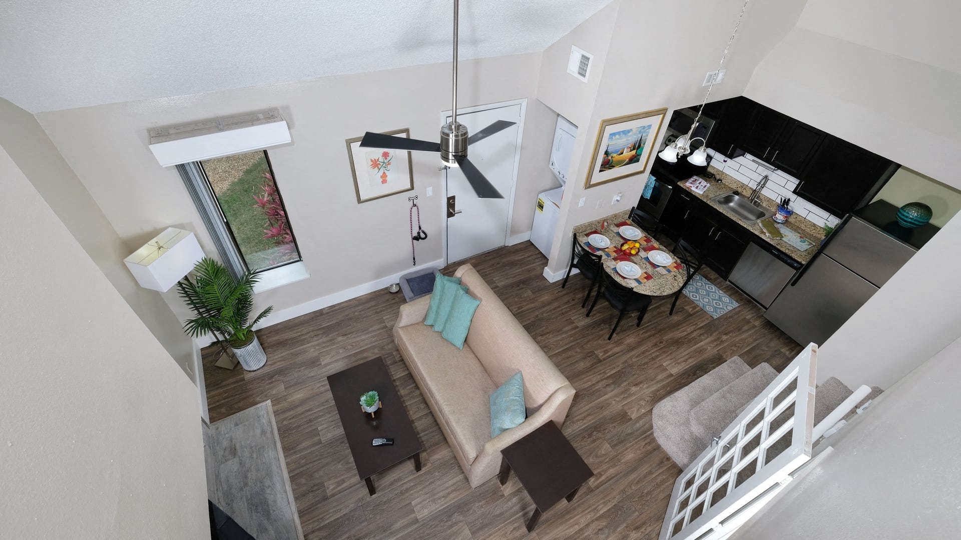 View of Fusion Orlando apartment living space from loft. Open concept living room and kitchen with ceiling fan and in unit laundry.