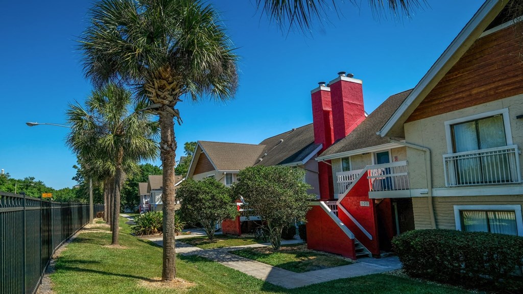 Street-facing Fusion Orlando apartments. Palm trees and a black iron fence line the main road and concrete paths lead to apartment doors.