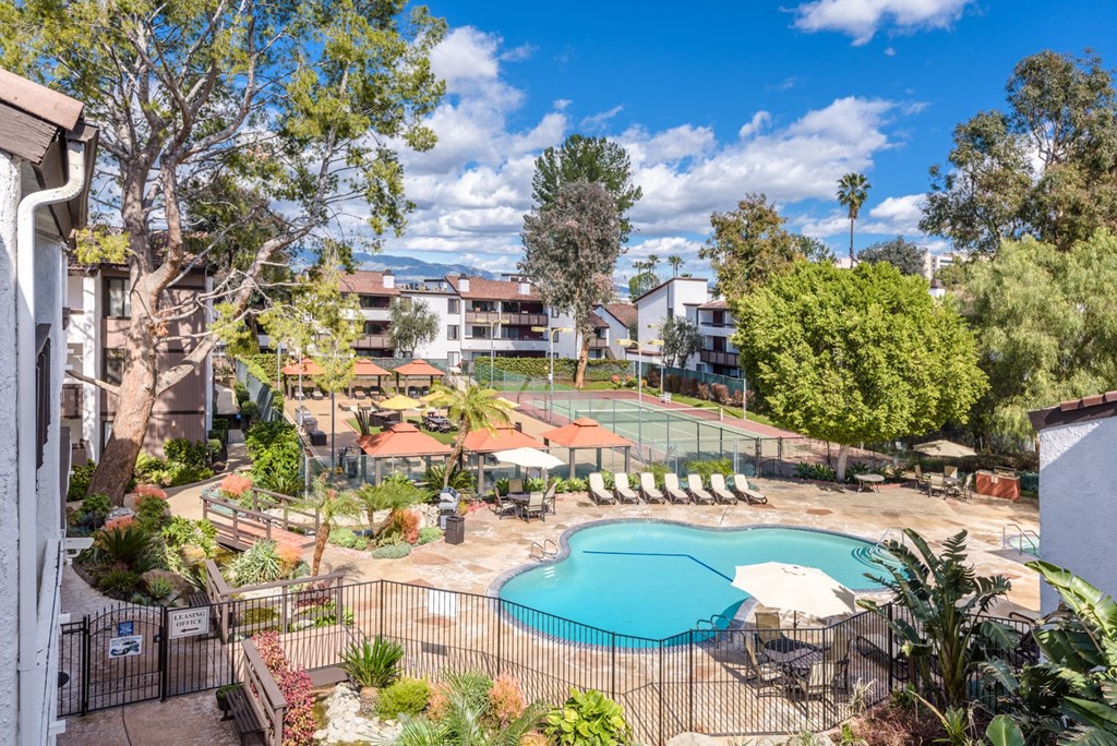 Fusion Warner Center apartments pool surrounded by black iron safety fencing next to tennis courts and courtyard with cabanas and lounge chairs.