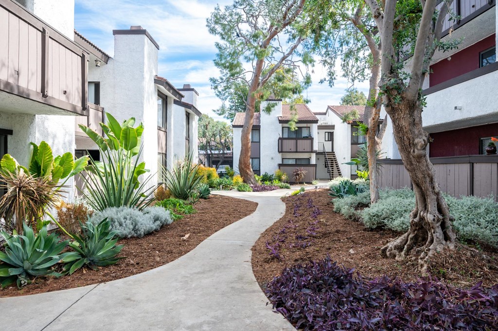 Fusion Warner Center apartments in Woodland Hills pathway between two-story buildings with lush green landscaping and brown bark mulch.