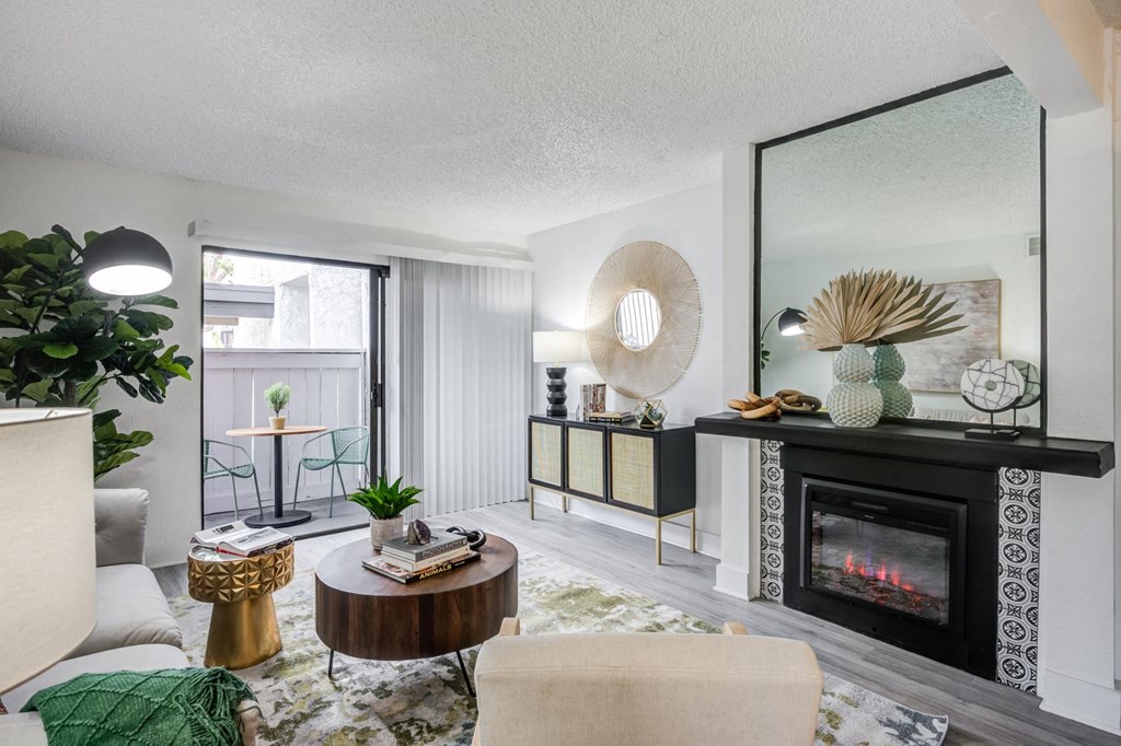 Fusion Warner Center apartments living room with elegant natural decor, electric tile fireplace and sliding glass door to patio.