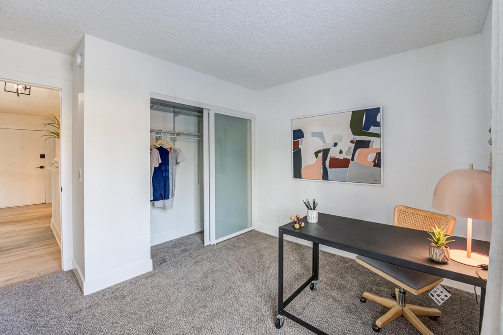 Fusion Warner Center two bedroom apartment in Woodland Hills carpeted office with minimalist desk, closet, and modern painting on wall.