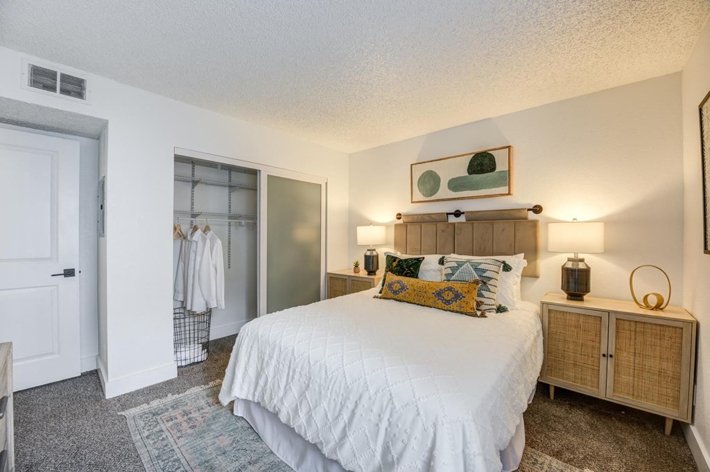 Fusion Warner Center one bedroom apartment in Woodland Hills carpeted bedroom with frosted glass doors on closet and large bed with white boho duvet.