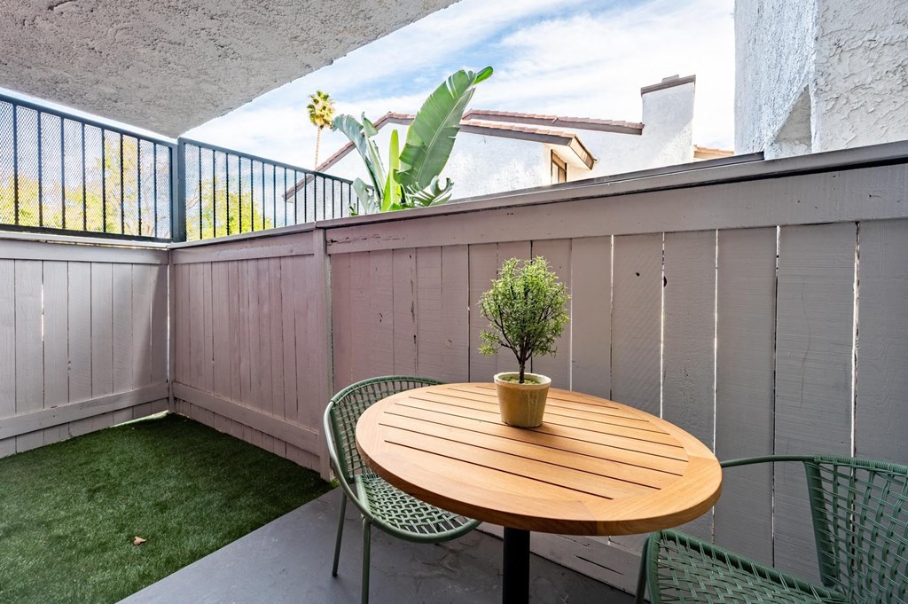 Fusion Warner Center apartments in Woodland Hills bottom floor patio with tall wooden fence, patch of lush grass, and modern patio table and chairs.