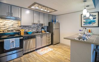 West Nashville Apartments - Retreat at Indian Lake - Modern Kitchen With Stainless Steel Appliances, Multicolored Tile Backsplash, Hardwood-Inspired Flooring, and a Breakfast Bar