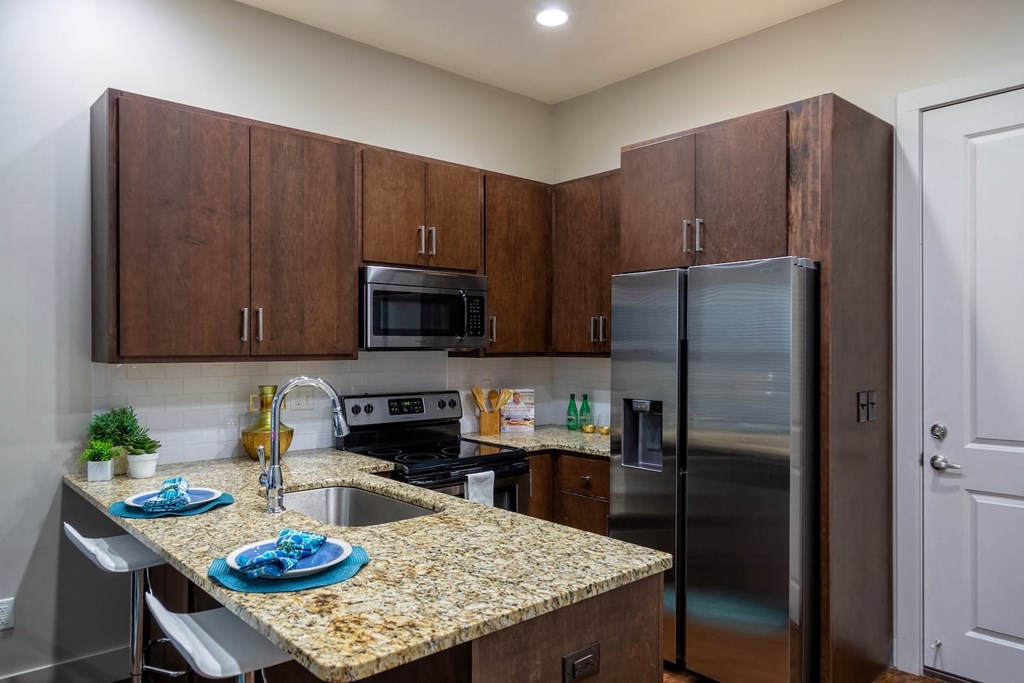 Kitchen in State Street Flats apartment in Nashville with stainless steel appliances, dark wood cabinets, and granite style countertops.
