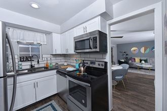 Lakeland, FL Apartments for Rent - Watermarc Apartments Kitchen with Stainless Appliances, Tile Backsplash, White Cabinetry, and Wood-Style Flooring