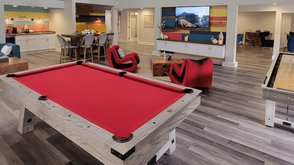 Fusion Orlando apartments clubhouse pool table with red felt and light grey wood in front of television center and next to coffee bar.