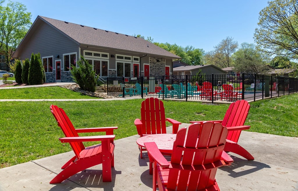 Outdoor seating area at the Retreat at Indian Lake apartments in hendersonville with four red Adirondack chairs around a matching table.