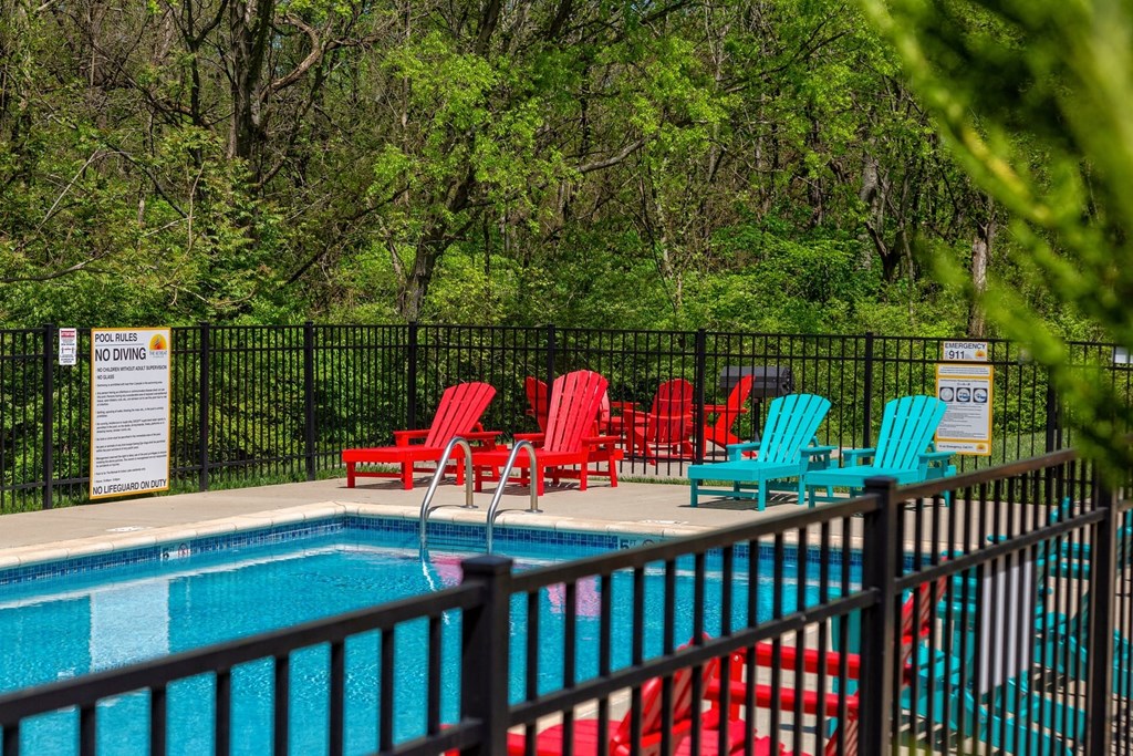 Community pool at the Retreat at Indian Lake apartments in hendersonville with red and blue lounge chairs and black iron fence.