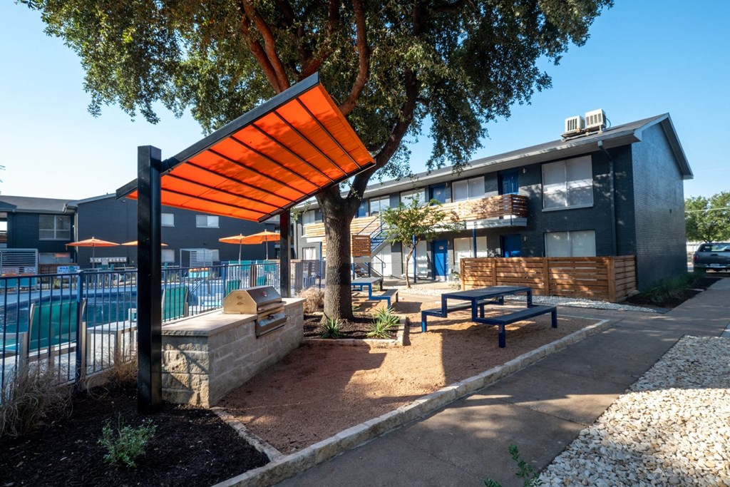 Poolside patio at Studio 700 apartments in Arlington, Texas with picnic table and grill with large prepping stations under an oak tree and large shade.