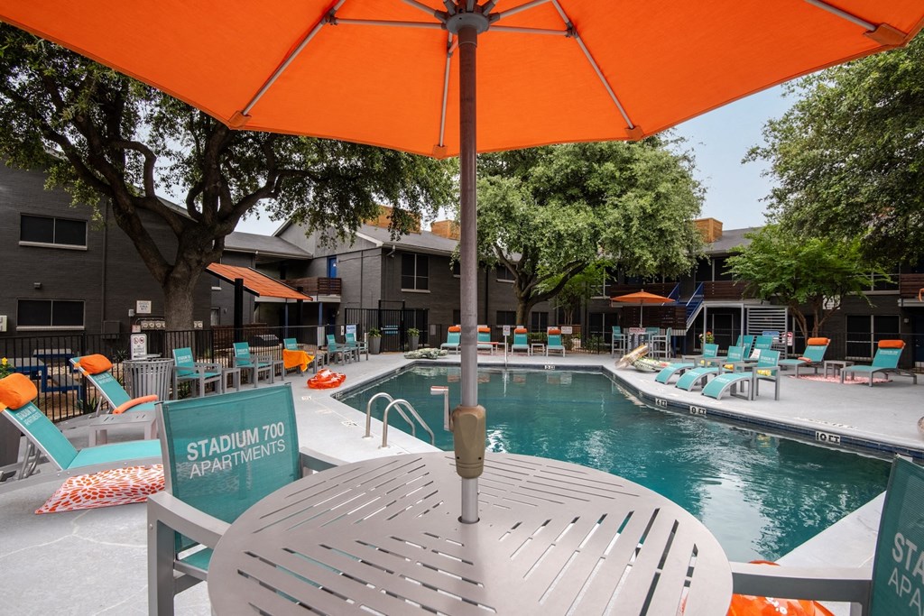 Large community pool and poolside table and chairs with orange umbrella at Stadium 700 apartments in Arlington, TX
