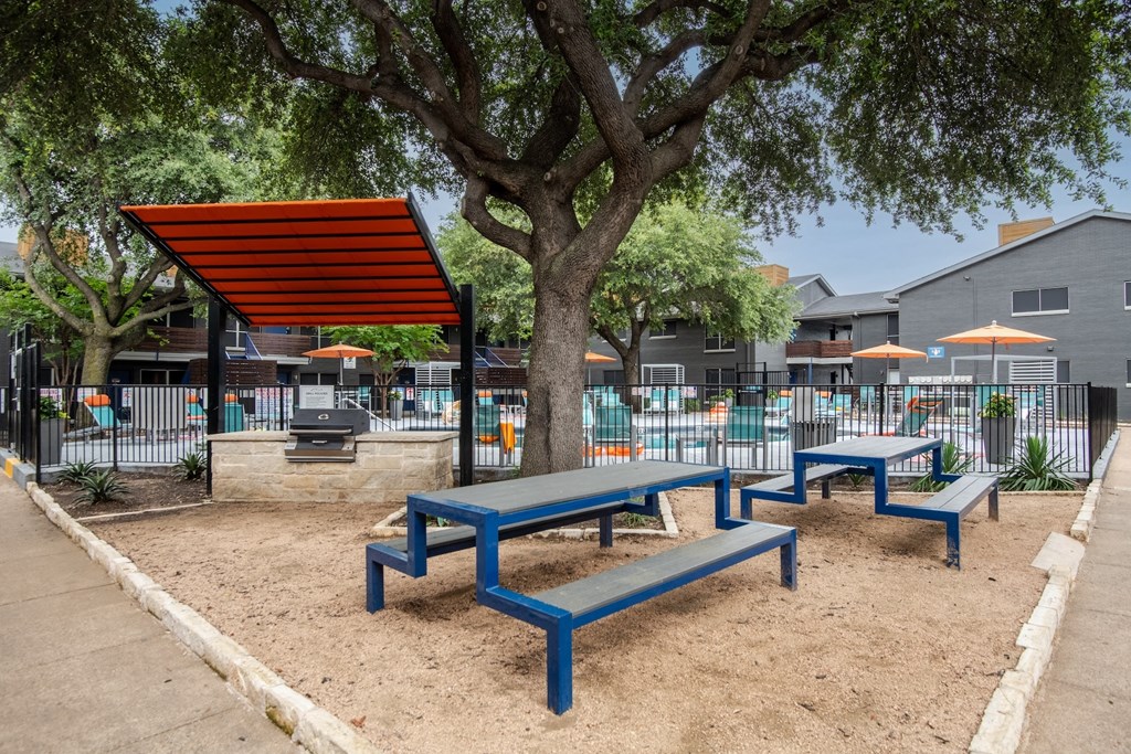 community grilling area at Stadium 700 apartments in Arlington, TX with picnic tables, large barbecue, and sun shade.