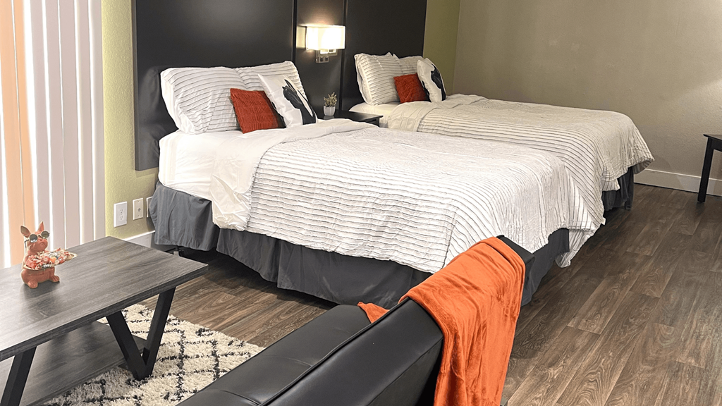 Fusion Orlando furnished studio apartment Orlando bedroom with two full beds. Beds have modern grey headboards, striped duvets, and orange and white pillows.
