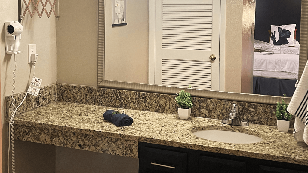 Fusion Orlando studio apartment kitchen bathroom vanity with long granite inspired countertop, double mirror, and single sink.