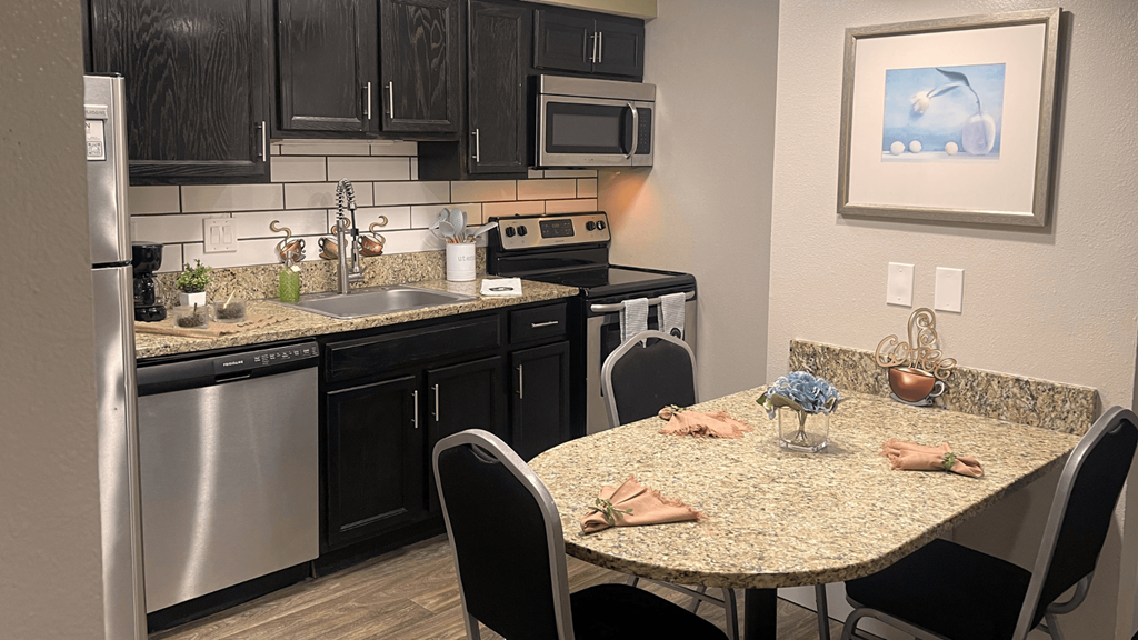 Fusion Orlando studio apartment kitchen with stainless steel appliances, espresso cabinets, and breakfast nook with three chairs.