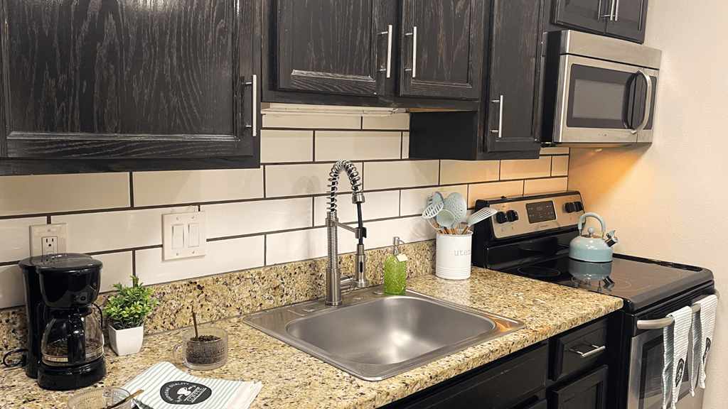 Fusion Orlando efficiency studio apartments in Orlando, Florida kitchen with espresso cabinets, electric stove, stainless steel microwave, and white subway tile backsplash.