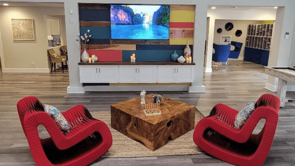 Fusion Orlando apartments lounge television on colorful pallet wall and two red modern rocking chairs around a wooden block coffee table.