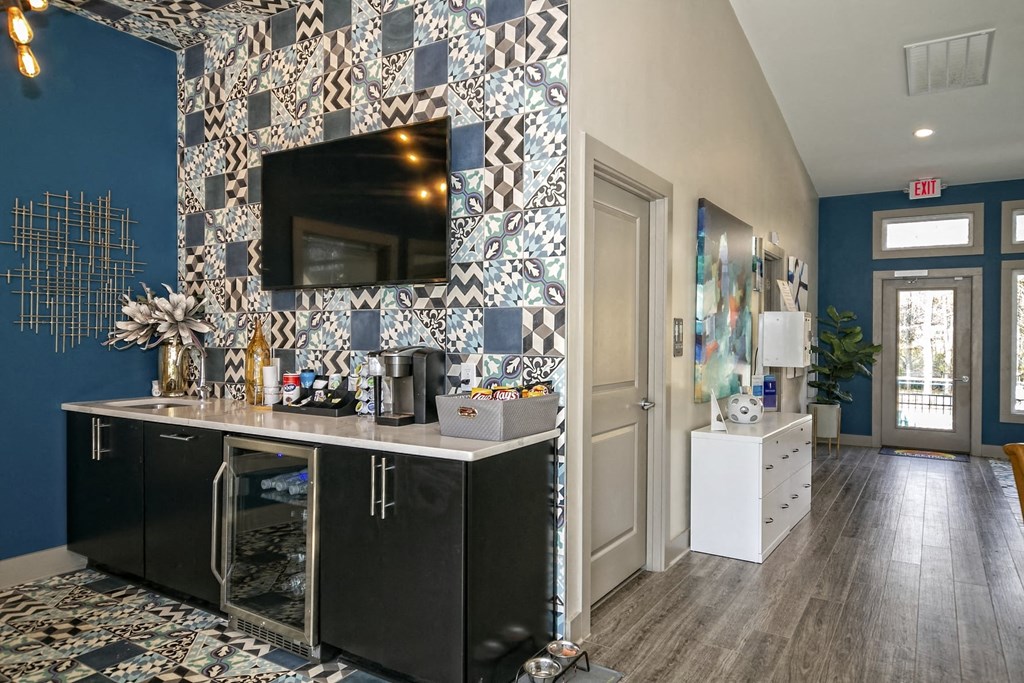 The Retreat at Indian Lake apartments lobby coffee bar with self-serve coffee supplies, black modern cabinets, and mini fridge.