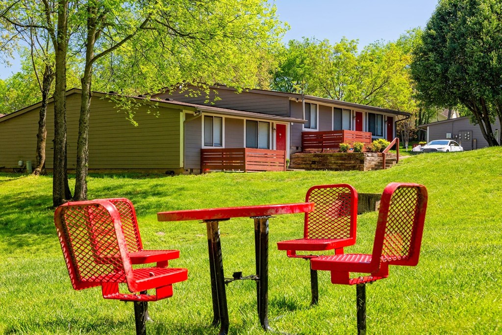The Retreat at Indian Lake grounds with red steel mesh picnic table and chairs on green lawn with apartments in background.