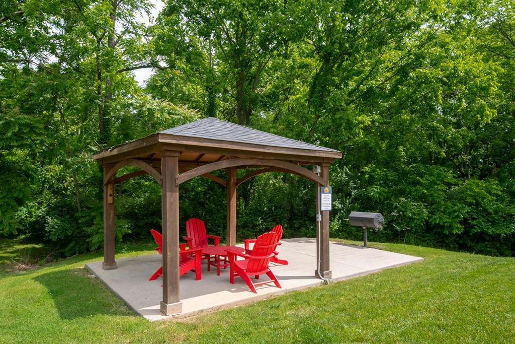 A wooden gazebo at The Retreat at Indian Lake Apartments in Hendersonville TN with red chairs is surrounded by greenery.
