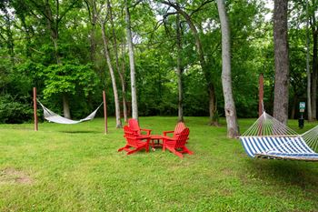 A red chair and a blue and white striped hammock are set up in a grassy area with trees in the background at the Retreat at Indian Lake Apartments in Hendersonville TN.