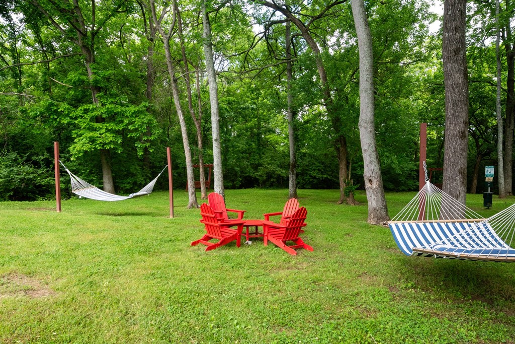 A red chair and a blue and white striped hammock are set up in a grassy area with trees in the background at the Retreat at Indian Lake Apartments.