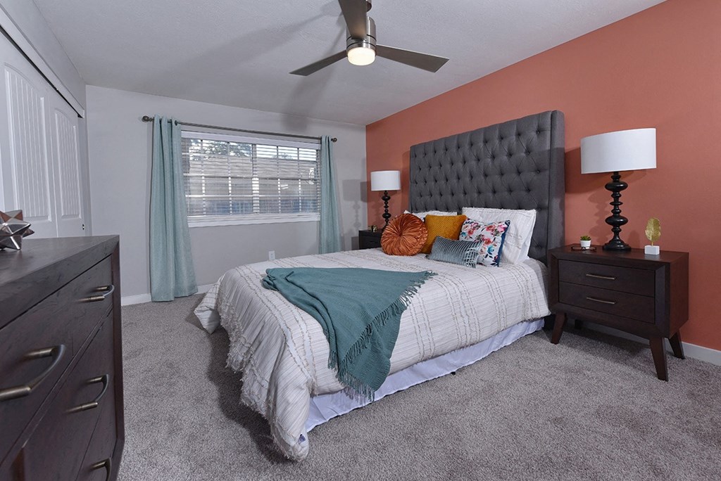 Bedroom One bedroom in Watermarc apartments Lakeland with luxury carpeting, salmon accent wall, and large window with blinds.