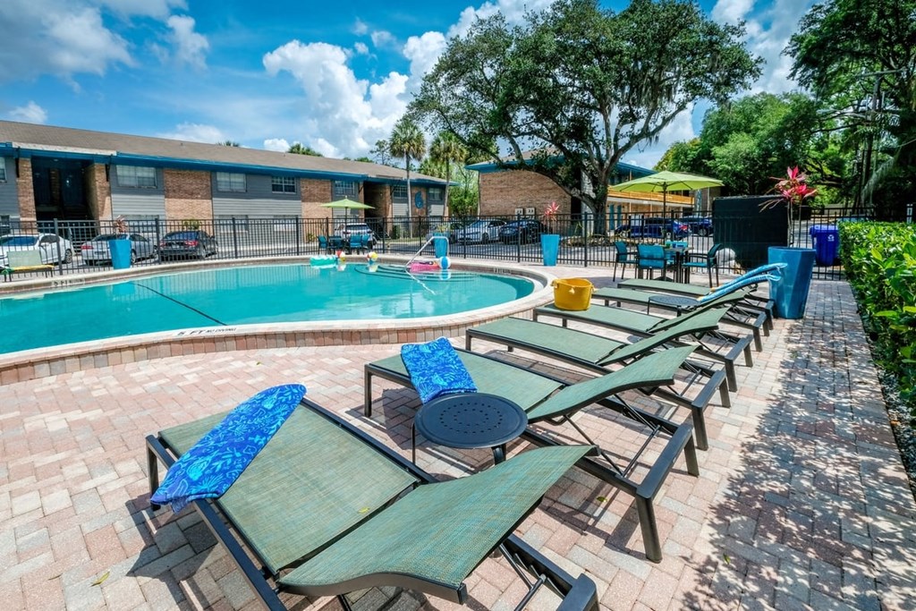 Green lounge chairs next to Community pool at the Watermarq luxury Apartments in Lakeland, Fl with metal side tables and tropical blue towels.